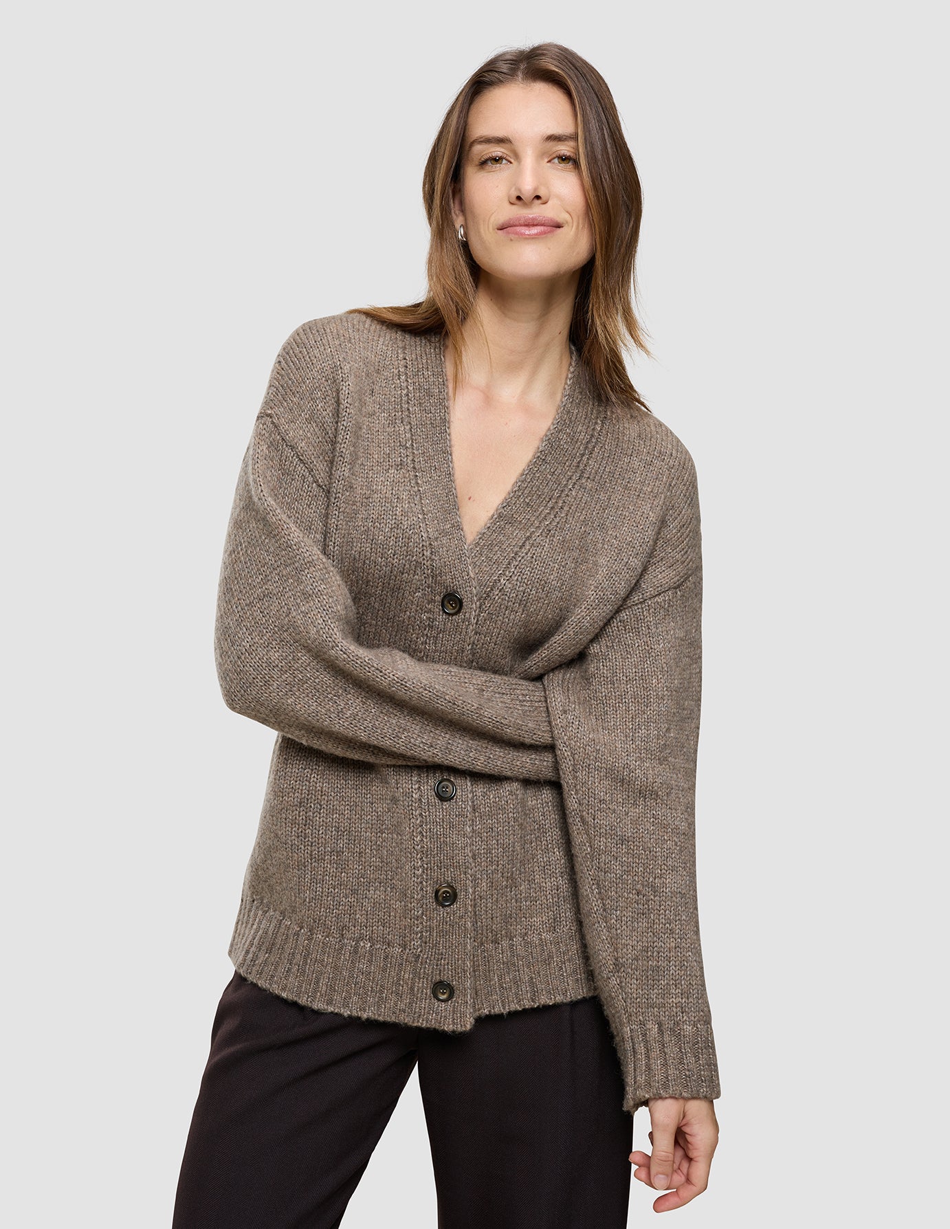 En kvinde iført en taupefarvet strikket cardigan med V-udskæring i blødt, groft uld i farven Taupe Melange i et klassisk dansk design.
