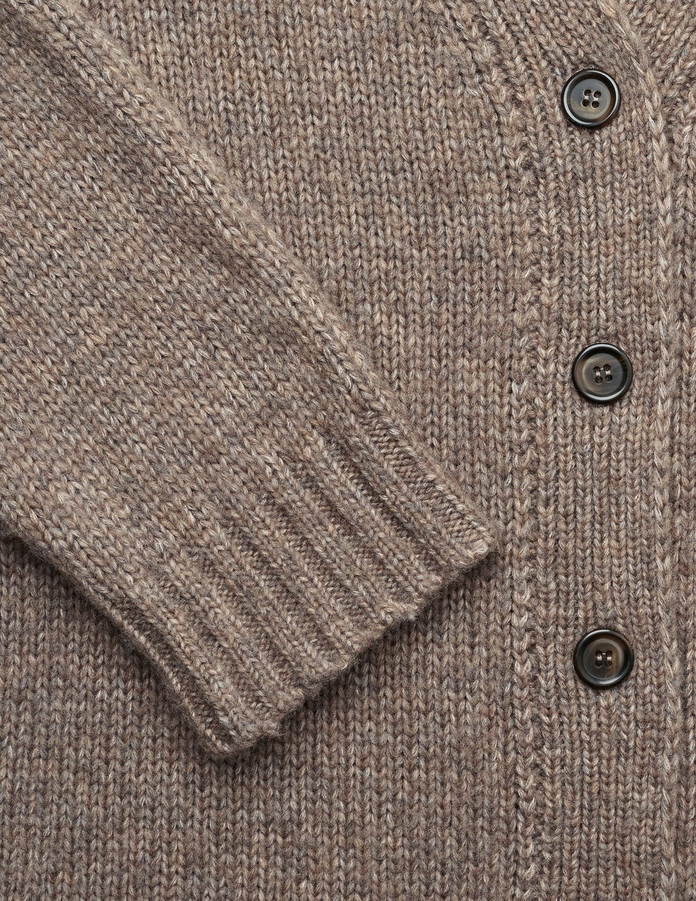 Nærbillede af en tyk, blød strikket cardigan til kvinder i taupe-melange med mørke knapper og ribkant ved håndleddene.