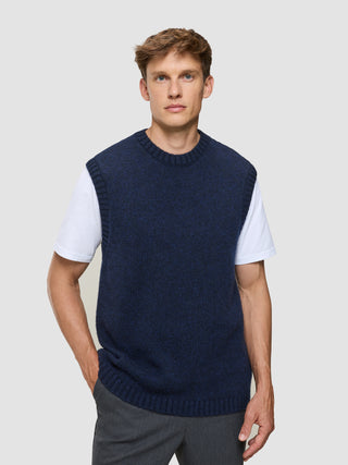 En mand har en tyk, blød uldstrikket vest i mørk marineblå melange på over en hvid T-shirt.