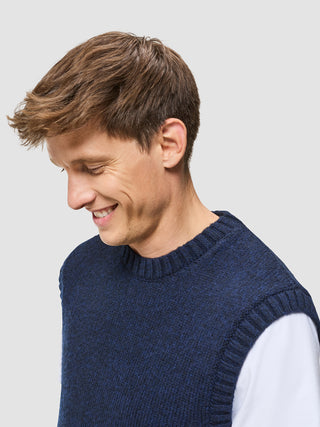 En smilende mand har en tyk, blød uldstrikket vest i mørk marineblå melange på over en hvid T-shirt.