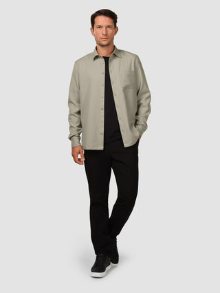En mand har en »Effortless Shirt« i farven »Stone Beige« på over en sort T-shirt og sorte bukser.