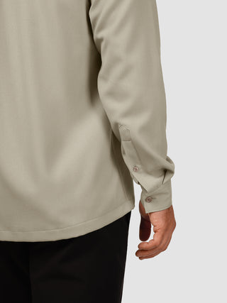 En person iført en »Effortless Shirt« i farven Stone Beige – en langærmet skjorte med knapper og manchetter.