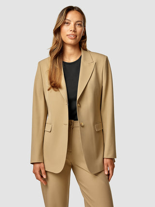 En kvinde iført en lysebrun Essential Blazer Caramel over en sort top.