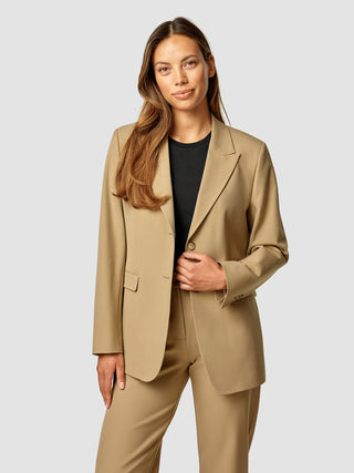 En kvinde iført en lysebrun Essential Blazer Caramel over en sort top.