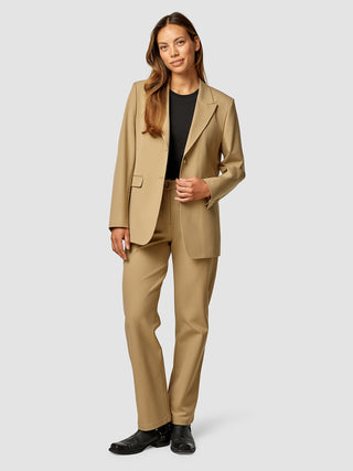 En kvinde iført en Essential Blazer i farven Caramel og matchende bukser over en sort top.