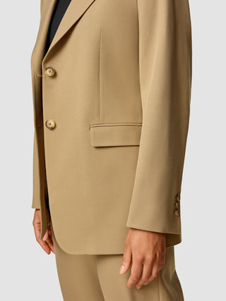 En person, der har en Essential Blazer i farven Caramel på over en sort bluse.