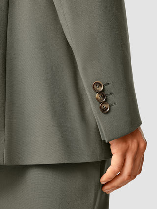 Nærbillede af ærmet på en Essential Blazer i mørk olivenfarve med tre brune knapper ved manchetten.