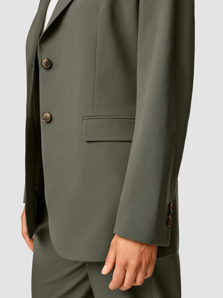 En person iført en Essential Blazer i farven Dark Olive med to knapper.