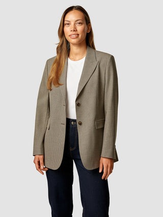En kvinde iført en Essential Blazer i farven Latte, en hvid T-shirt og mørke jeans.