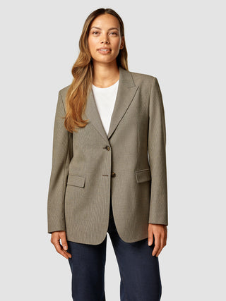 En kvinde iført en Essential Blazer i farven Latte, som hun har taget på over en hvid T-shirt og mørke jeans.