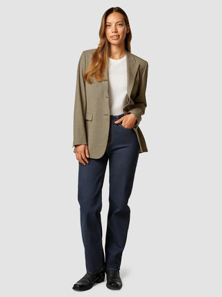En kvinde har en Essential Blazer i farven Latte på over en hvid T-shirt og mørkeblå jeans.