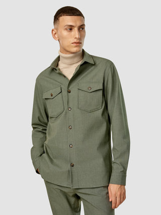 En mand har en Essential Overshirt i farven Nightfall Green Melange på over en beige rullekravebluse.