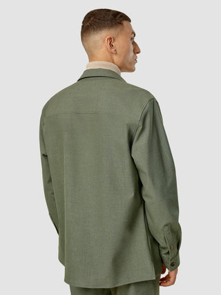 En mand set bagfra, iført en Essential Overshirt i farven Nightfall Green Melange over en rullekravebluse, i dansk design.