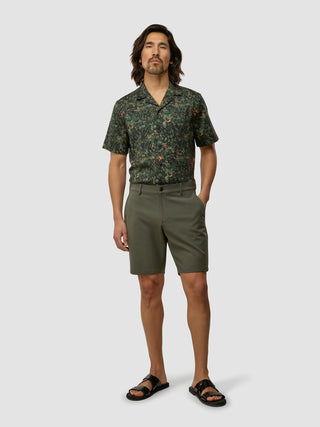 En mand iført en skjorte med botanisk mønster og GEN2™-shorts i farven »Muted Green« samt sorte sandaler.