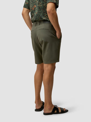 Set bagfra er personen iført en olivengrøn mønstret skjorte, GEN2™-shorts i farven »Muted Green« og sorte sandaler.