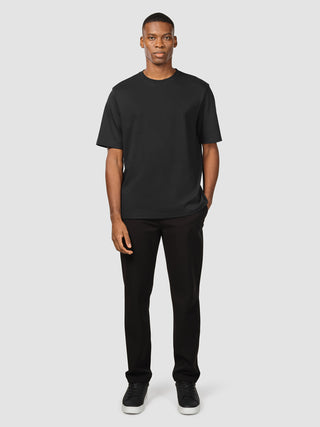 En mand iført en sort Heavy Box Fit-T-shirt, sorte bukser og sorte sneakers.
