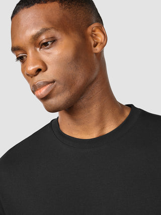 En mand iført en sort Heavy Box Fit-T-shirt ser ned.