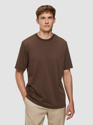 En mand har en Heavy Box Fit-T-shirt i farven Saddle Brown og beige bukser på for at skabe et afslappet look.