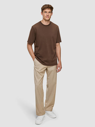 En mand iført en Heavy Box Fit-T-shirt i farven Saddle Brown, beige bukser og hvide sneakers.