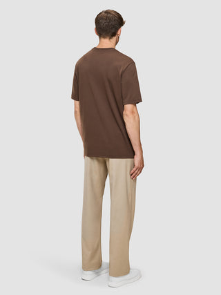 En mand set bagfra, iført en Heavy Box Fit-T-shirt i farven Saddle Brown, beige bukser og hvide sneakers.