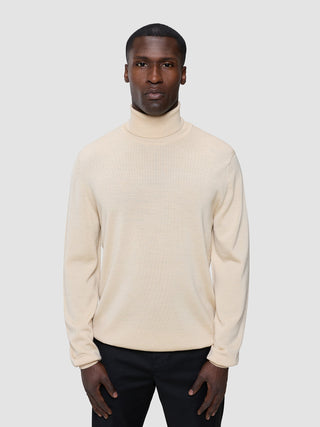 En mand iført en Seamless Premium Merino-strikket rullekravebluse i farven Birchwood.
