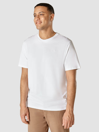 En mand har en Supima T-shirt i Box Fit Legacy White på med et lille broderet logo på brystet.