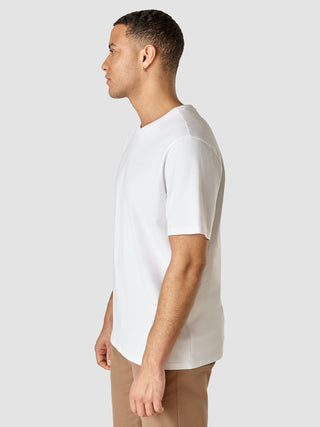 En mand set i profil iført en Supima T-shirt i Box Fit Legacy-modellen i hvid og beige bukser.