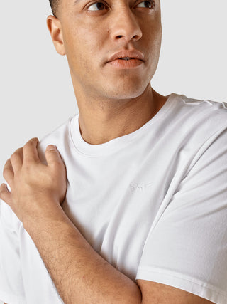 En mand iført en Supima T-shirt i Box Fit-modellen i farven Legacy White med diskret broderi på brystet.