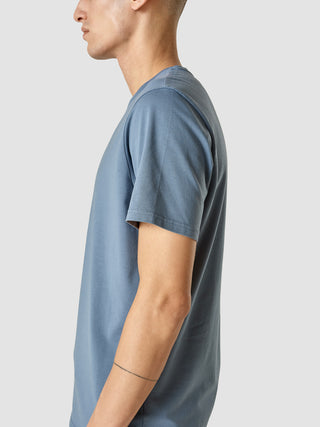 En mand set fra siden iført en Supima-T-shirt i farven Blue Mirage.