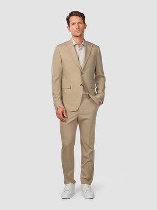 En mand iført et Tech Wool Suit Sand-jakkesæt, en lys skjorte og hvide sneakers.