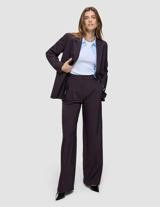 En kvinde iført en Avira Pants Wide Burgundy Berry-blazer til kvinder, som hun har taget på over en lyseblå skjorte og en hvid top.