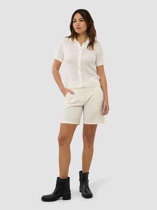 En kvinde iført en »Women’s Structured Polo Off White« med matchende shorts og sorte ankelstøvler.