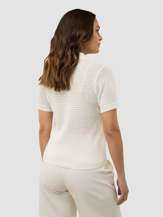 En kvinde set bagfra, iført en struktureret polo i farven »Off White« til kvinder og lyse bukser.