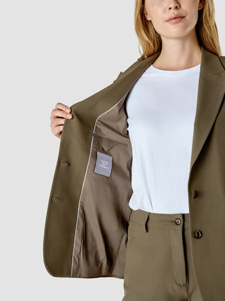En kvinde har en Essential Suit Straight Dark Olive-blazer på over en hvid T-shirt med et »Shaping new tomorrow«-mærke.