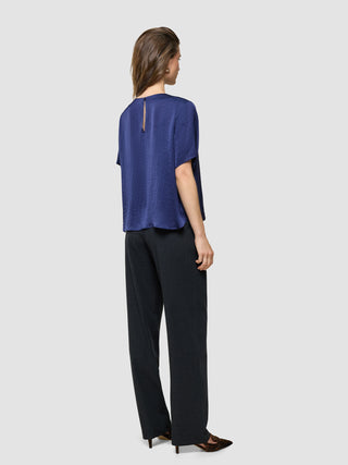 Amara Blouse i Navy, helfigur bagfra af kvinde i blå bluse og sorte bukser.