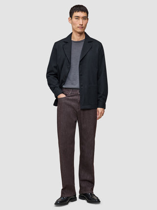En mand iført en mørkeblå Atelier-overshirt, en grå T-shirt, brune Atelier-bukser og sorte lædersko.