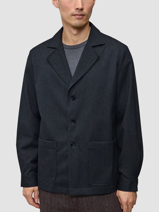 En mand bærer en Atelier Overshirt i mørk marineblå med en krave med udskæring, to påsatte lommer foran og en pasform i blazerstil.