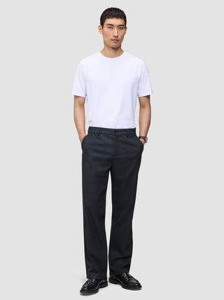 En mand i en hvid T-shirt, sorte loafers og Atelier Pants Relaxed Dark Navy, der er indbegrebet af afslappet dansk design.