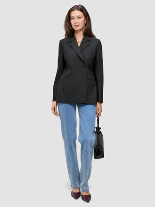 En kvinde iført en sort Avira-blazer til kvinder og blå jeans, der holder en lille sort håndtaske.