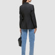 Bagfra-billede af en kvinde iført en sort Avira-blazer til kvinder, lysblå jeans og mørke højhælede sko, der holder en sort håndtaske.