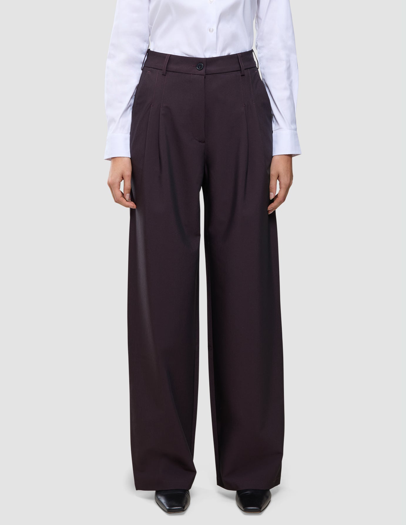 En person iført en hvid skjorte med knapper, der er stoppet ned i et par mørkeburgunderfarvede Avira-bukser til kvinder med høj talje i modellen Wide Burgundy Berry.