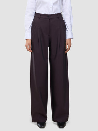 En person iført en hvid skjorte med knapper, der er stoppet ned i et par mørkeburgunderfarvede Avira-bukser til kvinder med høj talje i modellen Wide Burgundy Berry.