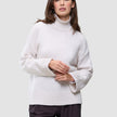 En kvinde har en Women’s Chunky Soft Wool Knit Turtleneck Sugar Melange på, en oversized, off-white trøje i grovstrikket design.