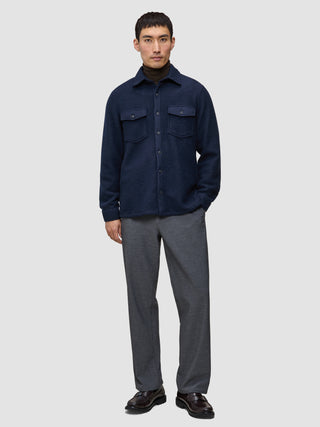 En person, der bærer en dobbeltlags uldskjorte i mørk marineblå i regular-pasform over en mørk sweater, grå bukser og mørke loafers.