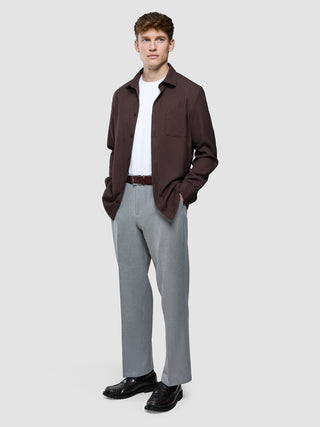 En mand har en mørkebrun Effortless-skjorte på over en hvid T-shirt, grå bukser og sorte loafers.