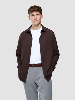 En mand iført en hvid T-shirt, en »Effortless Shirt« i mørkebrun og grå bukser.
