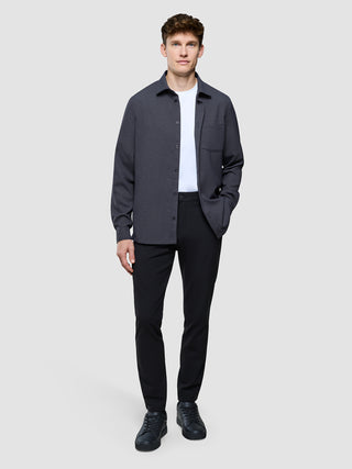 En mand har en let, vandafvisende Effortless-skjorte i mørkegrå på over en hvid T-shirt, sammen med sorte bukser og sneakers.