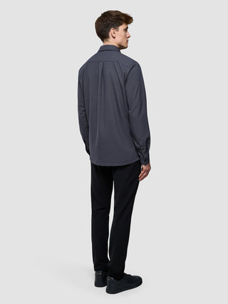En mand set bagfra, iført en koksgrå »Effortless Shirt Dark Grey«, sorte bukser og sorte sneakers.