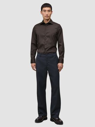 En mand har en mørkebrun Elevated Shirt Slim i Pima-bomuld på sammen med mørke bukser og fine sko.
