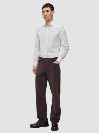 En mand iført en højtaljet, slim fit, lysegrå stribet skjorte, mørkebrune bukser og mørke loafers.